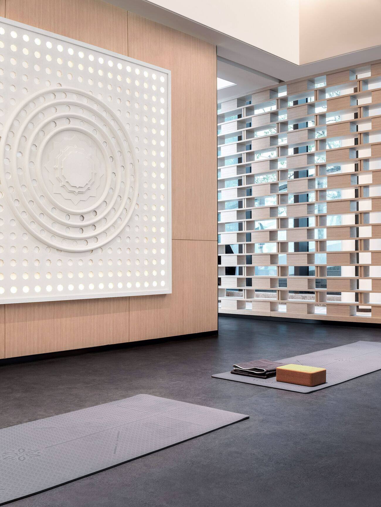 A minimalist yoga or meditation room with two mats on the floor, a wooden block and a large white circular wall sculpture
