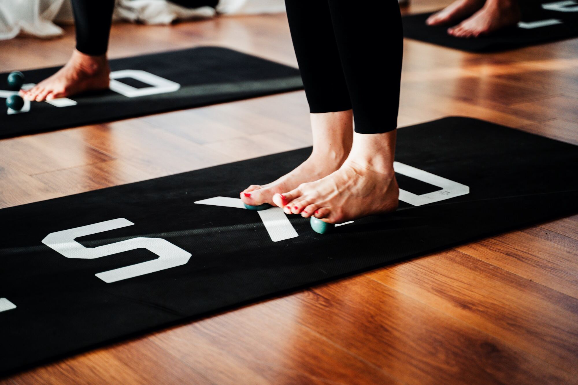 People standing barefoot on black yoga mats with white letters on a wooden floor