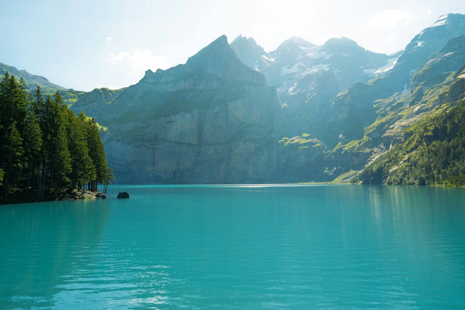 A turquoise alpine lake beneath steep, forested mountains under a bright sky