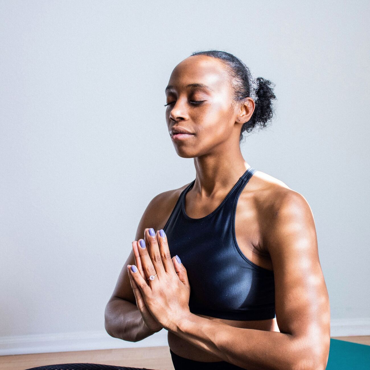A woman in athletic wear sitting with her eyes closed and her hands pressed together